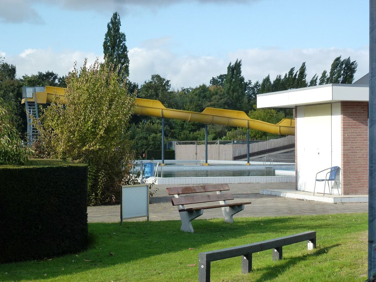 Buitenzwembad met gele glijbaan en een groen grasveld met bankjes